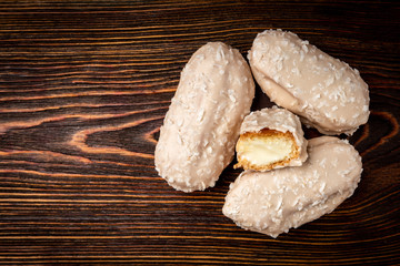 Coconut eclairs or custard cookies on dark wooden background.