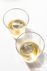 Two glasses of whisky with ice ball on white table