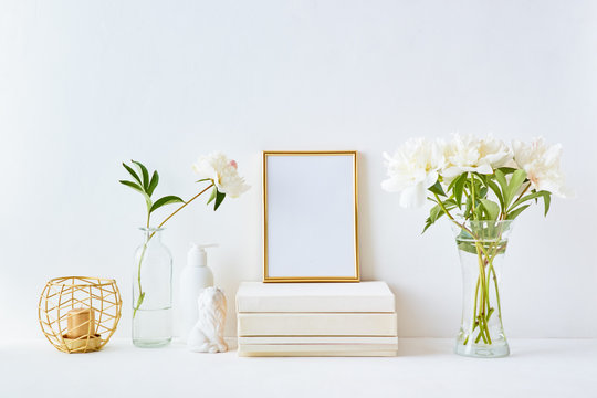 Home interior with decor elements. Gold frame, white peonies in a vase, interior decoration