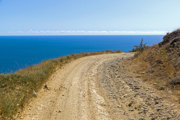 Fototapeta na wymiar A dirt road running along a deserted mountainside on the seashore.