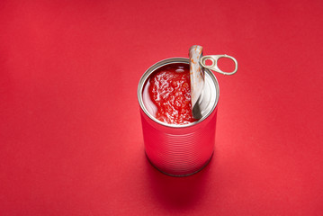 Opened tin can with canned tomatoes, on red background
