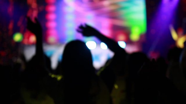 Slow motion,silhouettes of people partying, cheering and showing hands at rock concert in front of stage in big hall. Colorful blue stage lighting, Stage Spotlight with Led light.entertainment concept