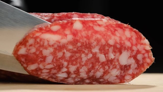 chef man slicing sausages salami on wood board closeup