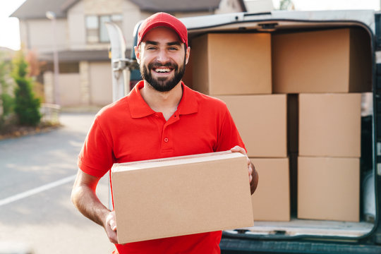 Image of smiling young delivery man standing with parcel box