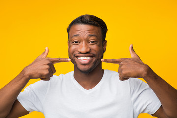 Joyful Afro Man Pointing Fingers At His Smile, Studio Shot