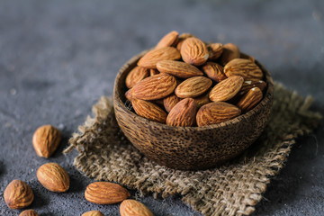Photo of almond in wooden bowl on gray background. Front View of almond. Almond with wooden spoon or scoop. On the table. Dark background. Images