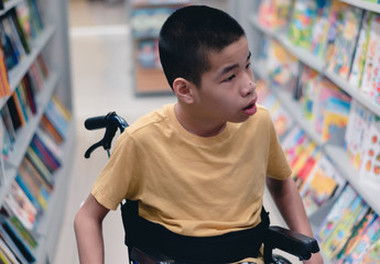 Disabled child on wheelchair having fun choosing books from shelves, Special children's lifestyle, Life in the education age of special need kids, Happy disability kid concept, Selective focus.