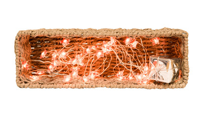 Christmas decoration. Wicker basket illuminated from inside with garland and shiny gift box. Isolated on white background. Subject of festive interior