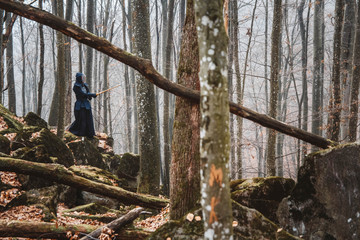 Man practicing kendo with shinai bamboo sword on rocks and forest background. Place for text or advertising