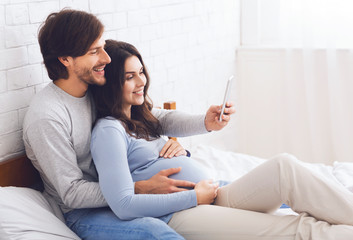 Pregnant couple relaxing with smartphone on bed at home