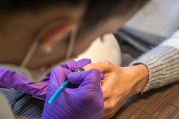 Beautician painting client's nails with black glitter nail polish. Close up.