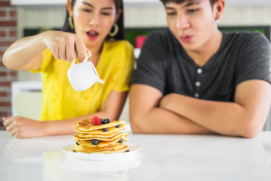 Young Asian man and woman couple sitting at dinner table woman pour sauce onto pancake, focus on pancake. - Powered by Adobe
