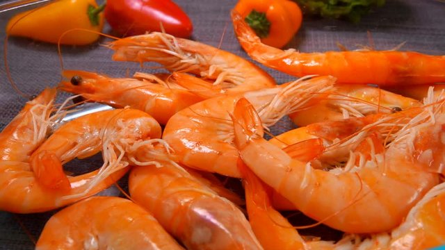 Hand lay delicious unpeeled shrimps in a glass bowl on the background of tomato and pepper