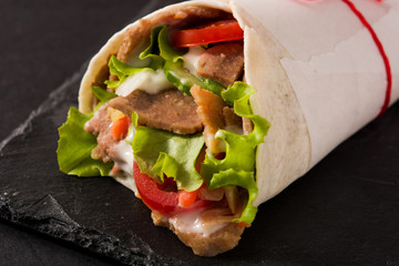 Doner kebab or shawarma sandwich on black slate background. Close up