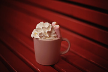 Dusty pink mug with coffee with cream and marshmallows on the red bench.