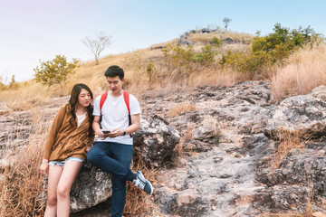 Happy romantic Couple Man and Woman using smartphone to find path to the destination on top of mountain and sitting on stone for rest. Landscape background. Adventure concept.