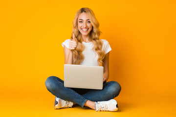 Cheerful woman using laptop and showing thumb up - obrazy, fototapety, plakaty
