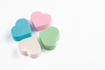 Assorted pink, blue, green and white pastel cosmetic sponges in heart shape on white background.