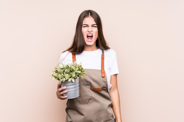 Young gardener caucasian woman holding a plant isolatedscreaming very angry and aggressive.