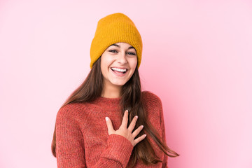 Young caucasian woman wearing a wool cap laughs out loudly keeping hand on chest.