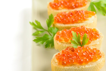 Slices of white bread with red fresh caviar and parsley on the white background closeup.