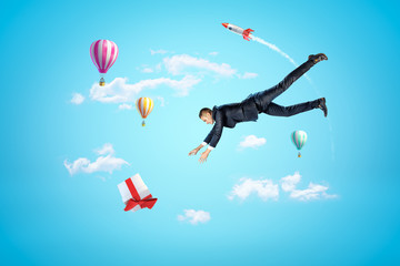 Businessman reaching to gift box with hot air balloons and silver red space rocket in the air on blue background