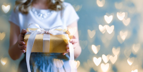 The woman's hands hold a gift box. Blue background with flickering light bokeh. Valentine's day,...