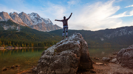 young woman doing gymnastics on a big rock at eibsee lake shore. evening scenery bavarian mountains