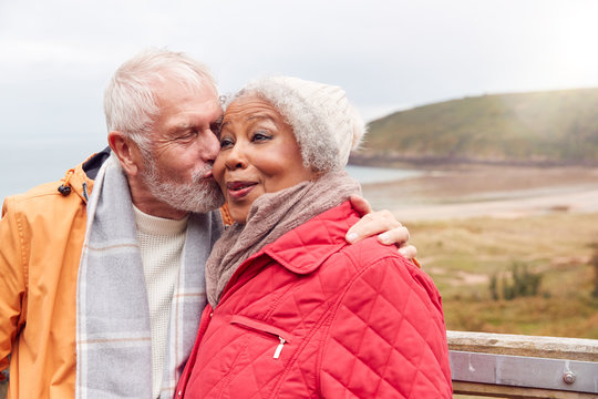 Loving Active Senior Couple Resting By Gate As They Walk Along Coastal Path In Winter
