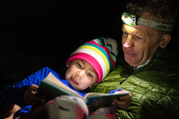 Family reading bedtime stories with headlamps on while camping.
