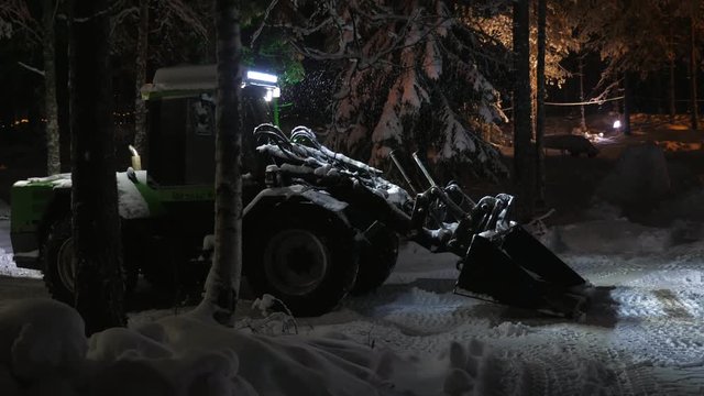 Up-to-date tractor with a big blaze cleaning wood in Finland at night in winter