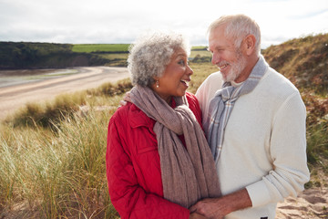 Loving Active Senior Couple Standing And Hugging On Walk In Sand Dunes On Winter Beach Vacation