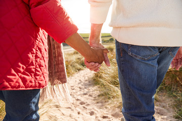 Close Up Of Loving Senior Couple Holding Hands Walking Through Sand Dunes On Winter Vacation - Powered by Adobe
