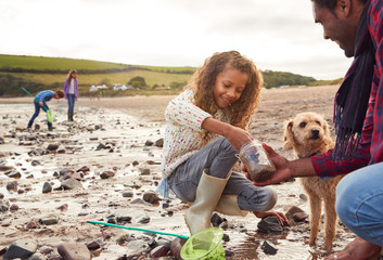 Family Looking In Rockpools On Winter Beach Vacation