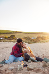 Loving Couple With Dog Relaxing By Fire On Winter Beach Vacation