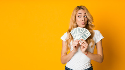 Pensive girl holding bunch of money banknotes and looking away