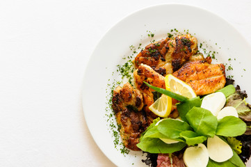 Delicious roasted chicken fillet served on a white plate with salad leaf aside. On a white background.