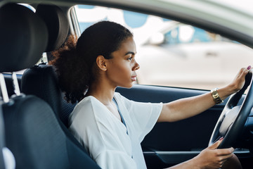 Side view of a woman sitting in a car holding a steering wheel and looking on the road