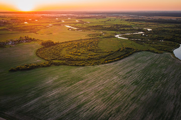 Fields and forests of Belarus at sunset a river flowing through the territory. View from above