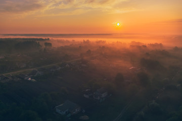 Aerial view - summer dawn in the fog over the village near the forest