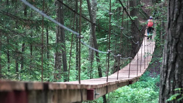 Man walking on a hanging bridge in National Park, USA. Stock footage. Rear view of a man hiker with backpack trekking in forest by hinged bridge