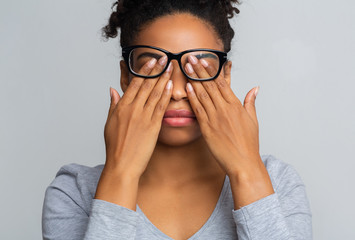 Black girl in glasses rubs eyes, suffering from tired eyes
