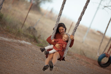 Happy mom and daughter swing on a wheel against the background of summer nature.