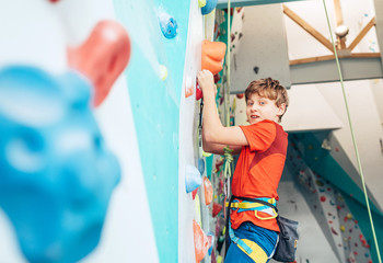 Smiling teenager boy at indoor climbing wall hall. Boy is climbing using a top rope,chalk bag and...