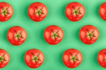 Creative pattern of colorful red tomatoes on green background. Concept of healthy food, creative cuisine, lifestyle and wellness.