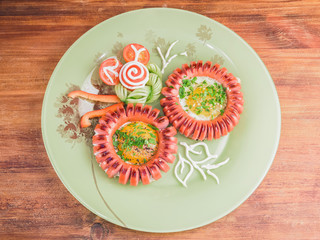 A romantic and fun breakfast for kids and loved ones. Creative fried scrambled eggs and flower shaped sausages with fresh vegetable salad on a green round plate on a wooden background
