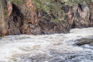 Fototapeta premium Red cliff, stone wall, forest, waterfall and wild river view in autumn. Fall colors - ruska time in Kiutaköngäs. One part of Karhunkierros Trail. Oulanka National Park, north Finland, Lapland, Europe