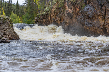 Red cliff, stone wall, forest, waterfall and wild river view in autumn. Fall colors - ruska time in Kiutaköngäs. One part of Karhunkierros Trail. Oulanka National Park, north Finland, Lapland, Europe