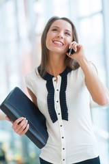 Businesswoman on mobile phone holding folder and smiling