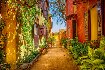 Street on Gorée island, Senegal, Africa. They are colorful stone houses overgrown with many green flowers. It is one of the earliest European settlements in Western Africa, Dakar - obrazy, fototapety, plakaty